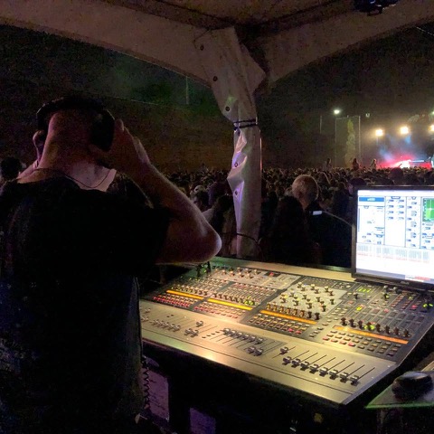 Stuart at a mixing console during a live show, looking out over a crowd