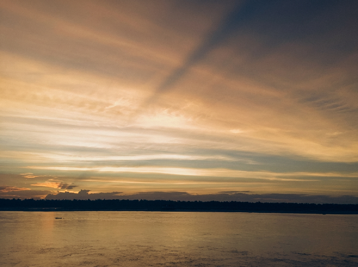 A calm sunset over still water, with a distant treeline under a golden sky