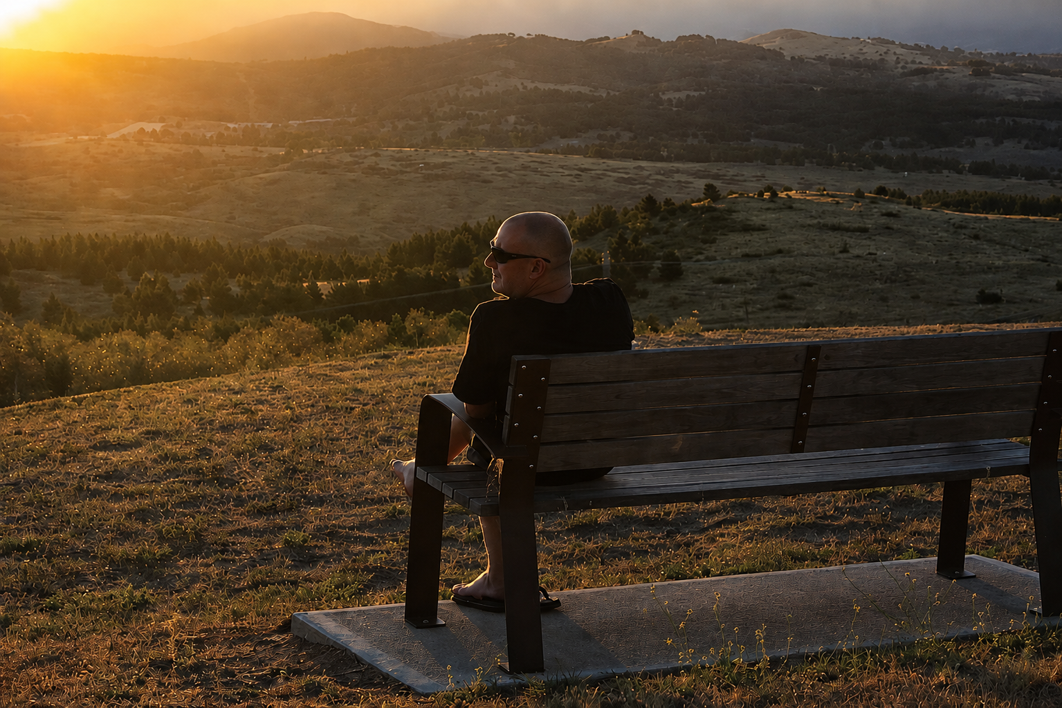 Stuart sitting on a bench at sunset, looking out over rolling hills and warm evening light
