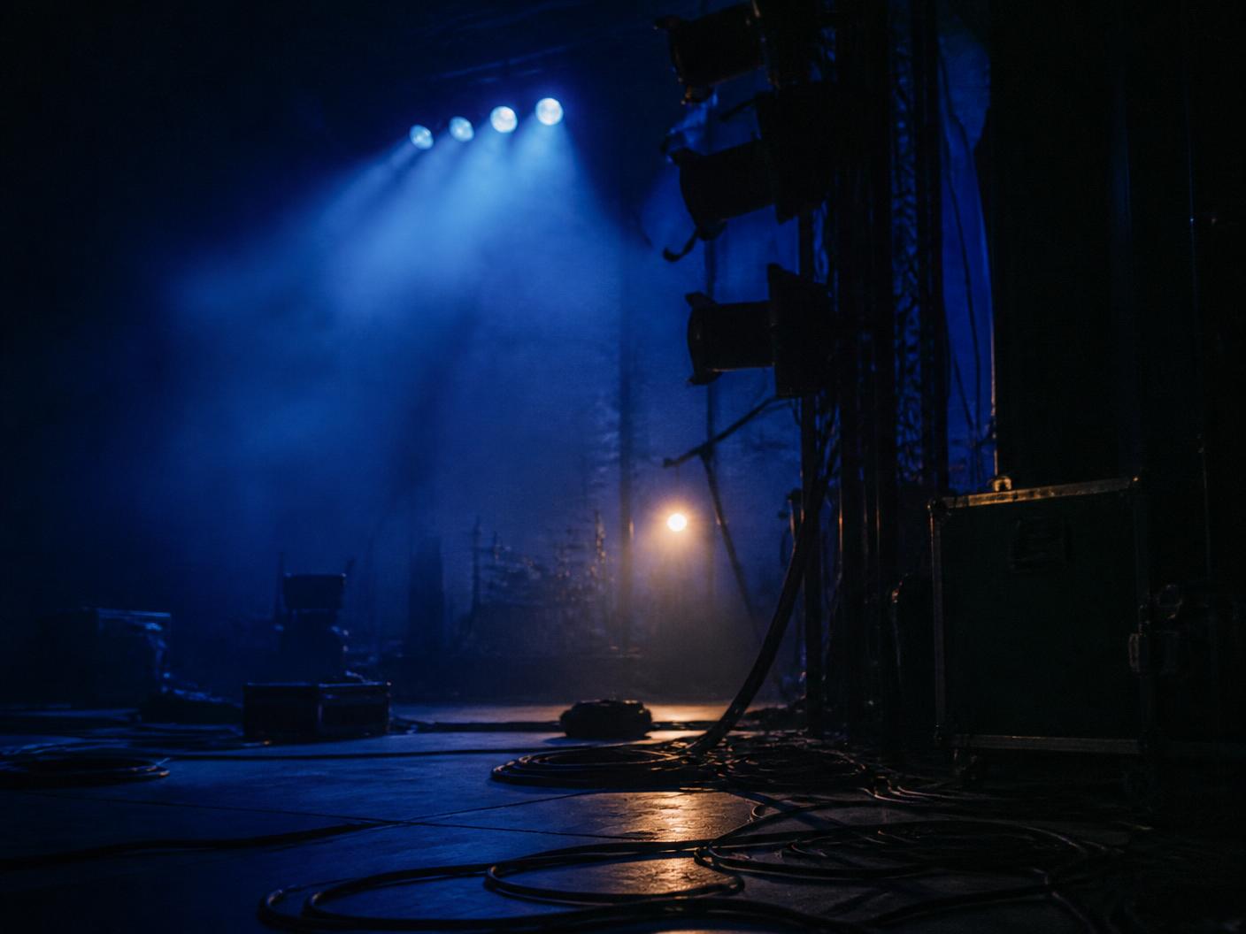 An empty stage after the show — lighting rig silhouettes, haze and coiled cables